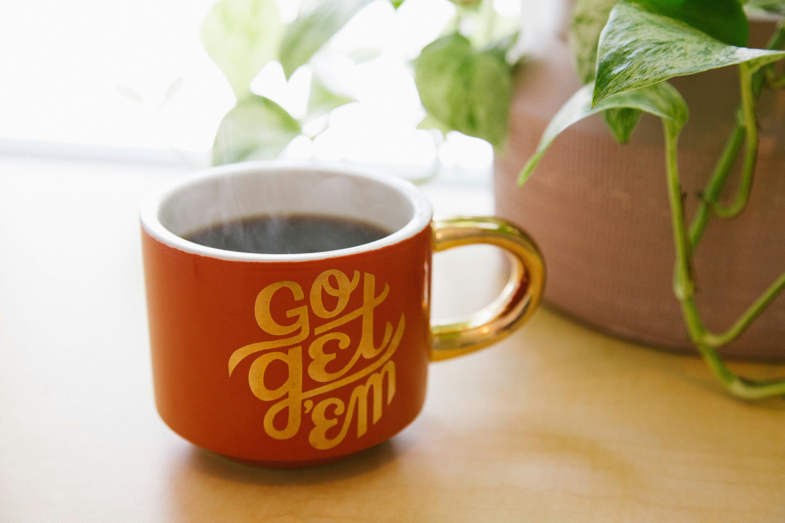 An orange motivational cup with a gold handle that say "Go Get Em".